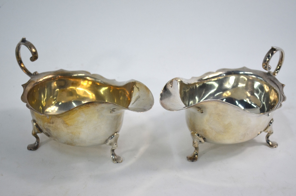 A near-matched pair of silver sauce boats with cut rims, scroll handles and pad feet,