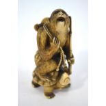 A stained ivory okimono carved as a Nihonzaru riding on the back of a tortoise in a parody of