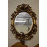 A decorative oval gilt framed wall mirror surmounted by a cherub