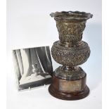 A Burmese white metal vase on cylindrical wood stand with presentation plaque,