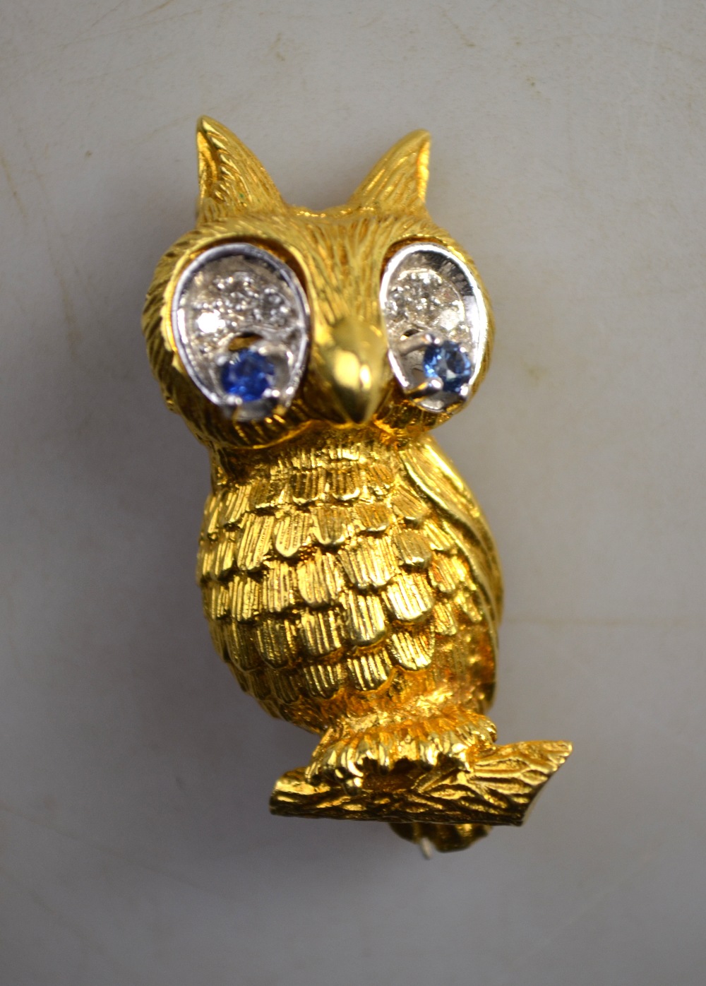 An 18ct yellow gold owl brooch with sapphire and diamond eyes, realistically textured,