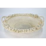 An early Belleek oval basket weave twin handle dish decorated in bold relief with flowers and