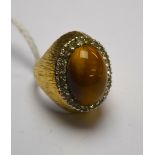 An oval cocktail ring set with large cabochon tiger's eye with white stones around,