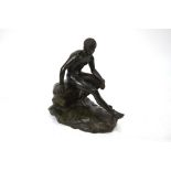 A patinated bronze cast figure of a classical young man seated on a rocky outcrop,