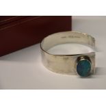 A contemporary open style bangle set with oval opal, stamped STG.