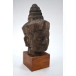 An imitation stone head of a Deity in the Khmer style, mounted on a wood stand,
