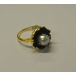 A single cultured pearl ring set within flower open flower with black petals,