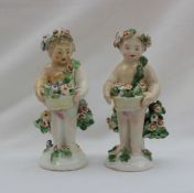 A pair of Derby cherub figurines holding a basket of flowers with flowers and leaves around,