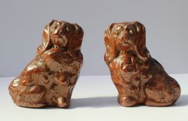 A pair of stoneware figures of Spaniels with a treacle glaze,