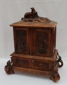 A Black Forest carved oak table top cabinet, the surmount carved with goats,