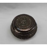 An Indian white metal box and cover of circular form the lid embossed with a seated figure,