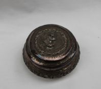 An Indian white metal box and cover of circular form the lid embossed with a seated figure,