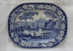 A 19th century blue and white pottery meat plate decorated with a river scene with a church beyond,