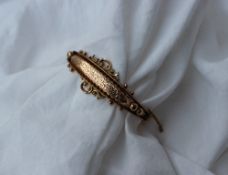 A 9ct yellow gold hinged bangle with a leaf engraved panel and ball and scrolls, marked 9ct,