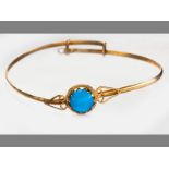 A YELLOW GOLD AND TURQUOISE BANGLE, in claw-set turquoise flanked by scrolls on solid bangle with