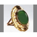 A 9CT YELLOW GOLD AND JADE RING, the oval jade in tube setting on stepped oval form, split shoulders