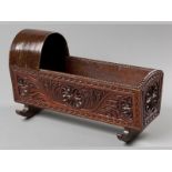 A VICTORIAN STAINED PINE DOLLS CRADLE, with a hooded shade over heavily carved canted panels, on