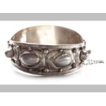 A SILVER BANGLE, embellished with oval and circular forms, ending in a tongue clasp with safety