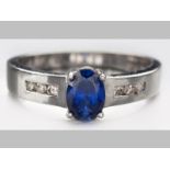 A 9ct WHITE GOLD, BLUE SAPPHIRE AND DIAMOND RING, oval sapphire claw set with channel set diamond