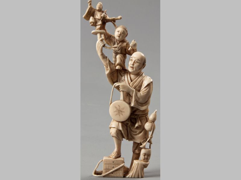 A 19TH CENTURY JAPANESE IVORY OKIMONO, the standing street entertainer accompanied by a boy on his