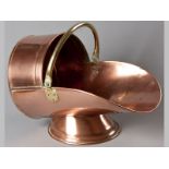 AN EDWARDIAN COPPER COAL SCUTTLE, of inverted helmet form, with a brass swing handle, standing on