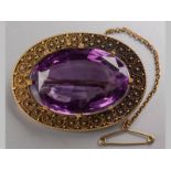 A 15CT GOLD AND AMETHYST BROOCH, the large oval amethyst in an oval rope, scroll and floral frame,