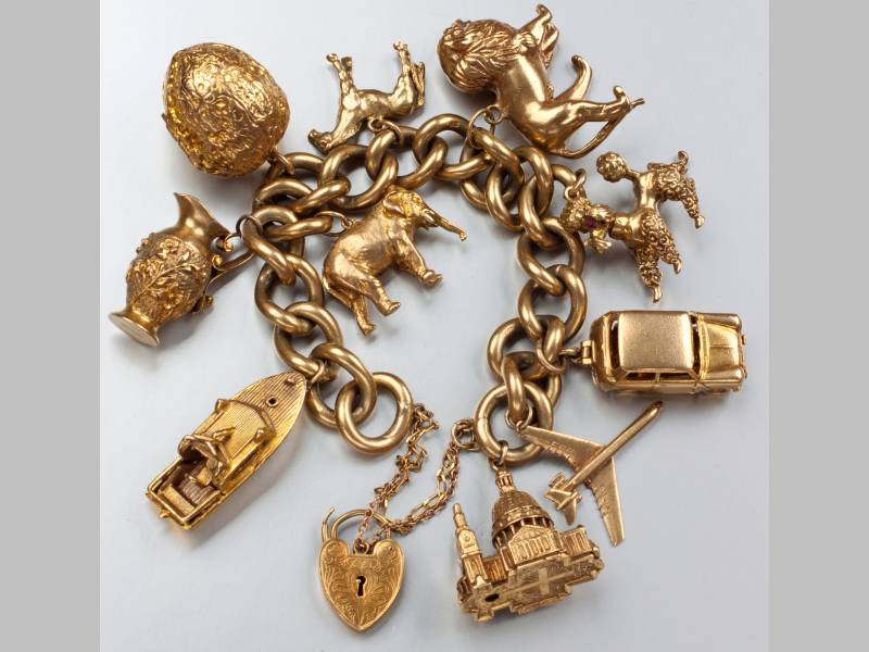 A 9CT YELLOW GOLD CHARM BRACELET, with large curb links, comprising of ten large charms to include