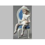 A LLADRÓ FIGURINE OF A YOUNG HARLEQUIN, seated on a French chair whilst holding a cat, base with