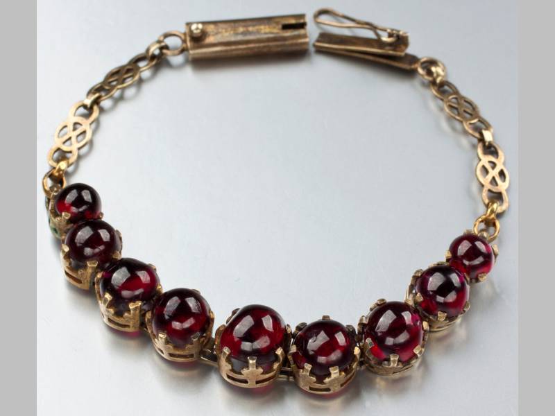 A 9CT YELLOW GOLD AND GARNET BRACELET, claw-set with nine cabochon garnets, ending in a tongue clasp