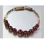 A 9CT YELLOW GOLD AND GARNET BRACELET, claw-set with nine cabochon garnets, ending in a tongue clasp