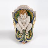 Fayence-Konsole mit Putto. Wohl 18. Jh. Ungemarkt. Schwere Wandapplik als geschweiftes Konsolbrett