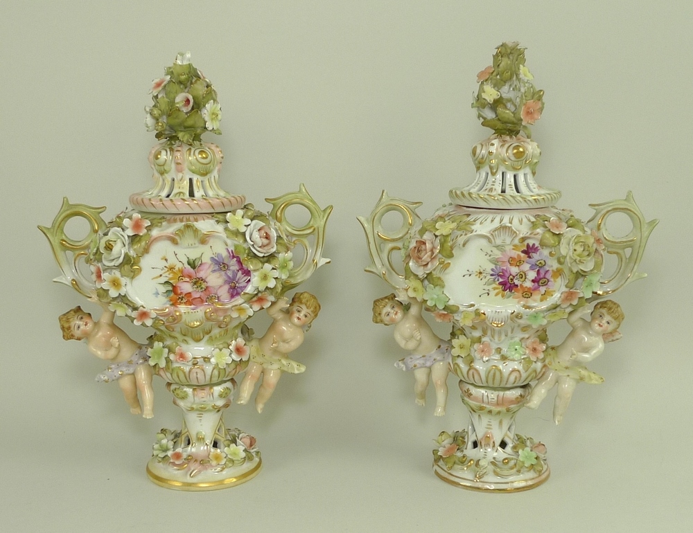 A pair of Sitzendorf lidded vases, decorated in high relief with flowers and pair of putti,