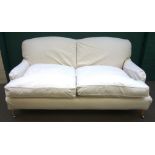 A Howard style three seat sofa, with loose cream upholstery, on turned supports,