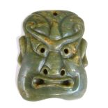 A Chinese jade mask, carved as a grimacing face, with pierced eyes, nostrils and mouth, 15cm.high.
