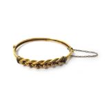 A gold oval hinged bangle, the front in a beaded and interwoven design, on a snap clasp,