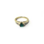 A white gold, emerald and diamond ring, claw set with a circular cut emerald at the centre,