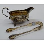 A George III silver sauceboat, with a decorated rim, scrolling handle and raised on three feet,