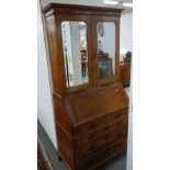 A George II figured walnut bureau cabinet with bevelled mirror doors over fitted interior and two
