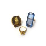 A gold ring, claw set with a large rectangular step cut smoky quartz, between decorated shoulders,