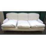 A Howard style three seat sofa, with loose cream upholstery, on turned supports,