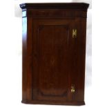 A George III oak and mahogany wall hanging corner cabinet, fitted with shaped shelves,
