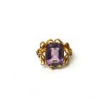 A gold ring, claw set with a cut cornered rectangular step cut amethyst, between pierced shoulders,