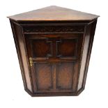 A reproduction oak corner cabinet, early 20th century, enclosed by a panelled door, 64cm wide.