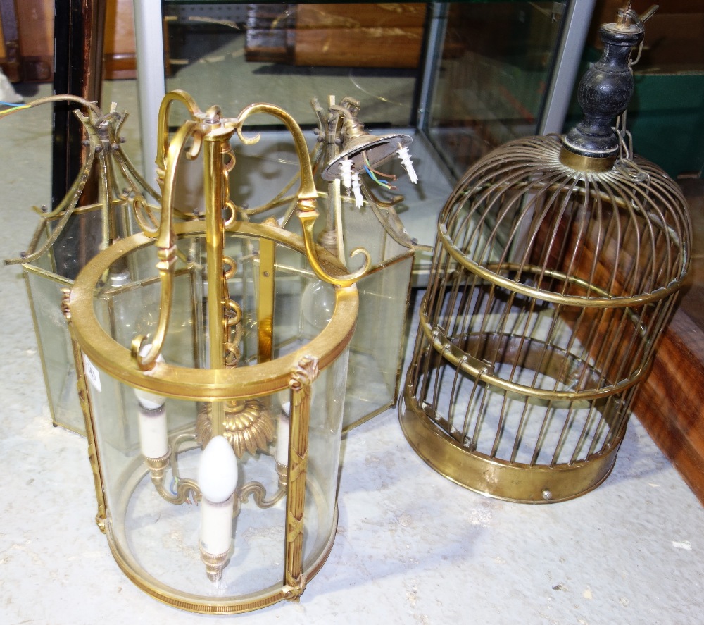 A group of three gilt metal and glass hanging lanterns and a brass bird cage, (4).