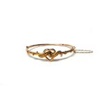 An Edwardian gold oval hinged bangle, the front with an open heart and beaded scrolling motif,