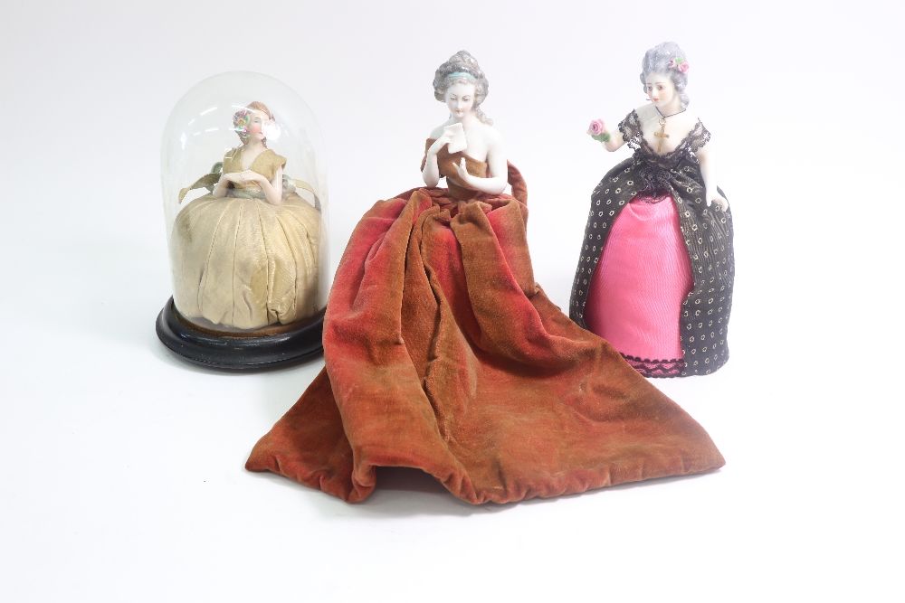 Three porcelain pin cushion dolls, late 19th century, modelled as ladies, one holding a letter,