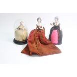 Three porcelain pin cushion dolls, late 19th century, modelled as ladies, one holding a letter,