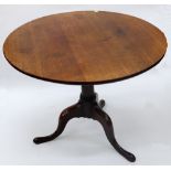 A George III oak tea table, the circular tilt-top on a gun barrel pillar and tripod base,