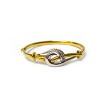 A two colour gold and diamond set oval hinged bangle, the front in a pierced scrolling design,