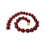 A single row necklace of reconstituted red amber uniform beads, on a spherical snap clasp,